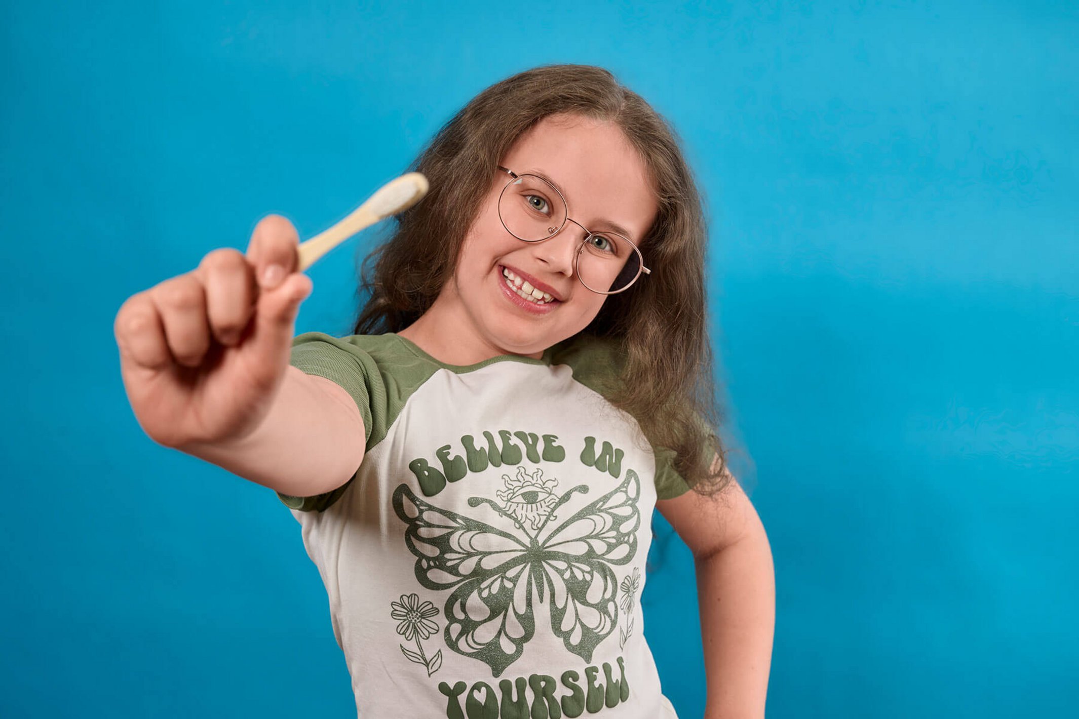 Ein junges Mädchen mit Brille hält eine Holzzahnbürste in die Kamera